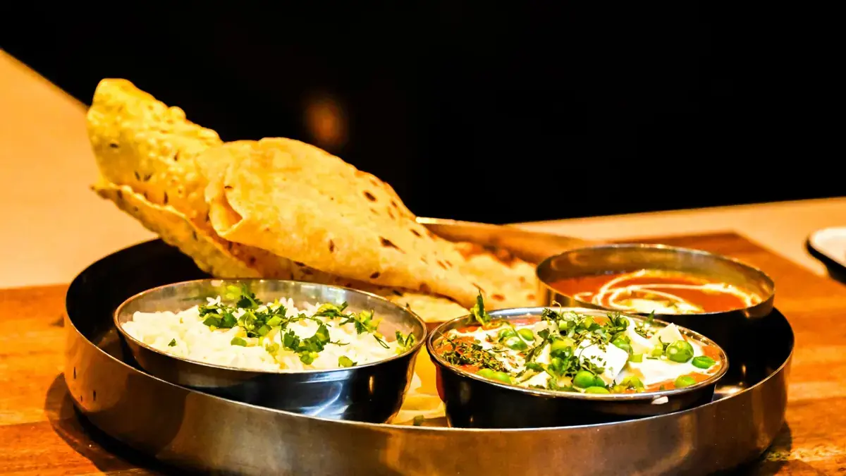 Photo: Exquisite Indian thali with naan bread, paneer curry, and aromatic rice served on a wooden table.